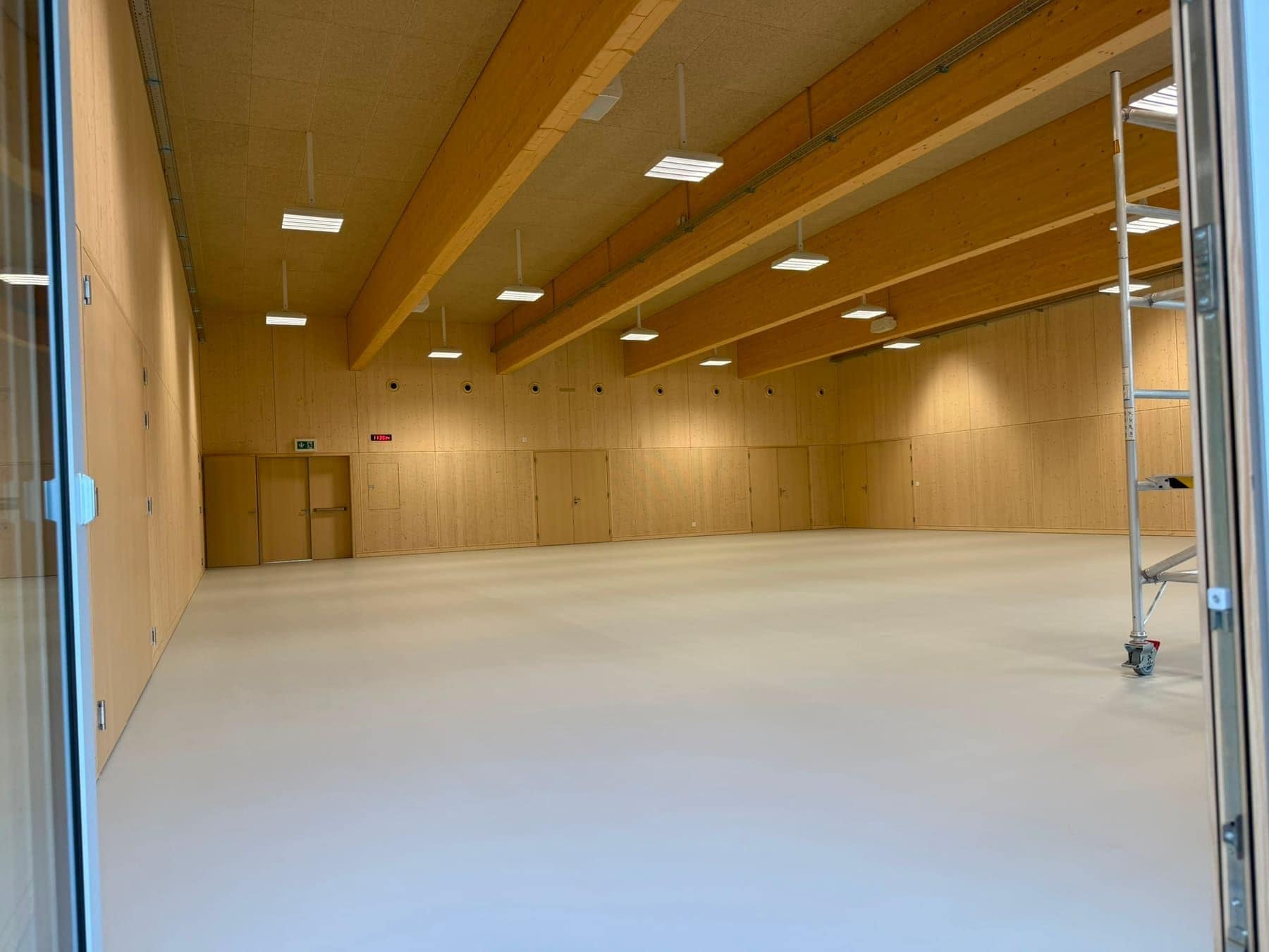 Leerer Saal mit Holzdecke und hellem Boden, am Rand ein Rollgerüst