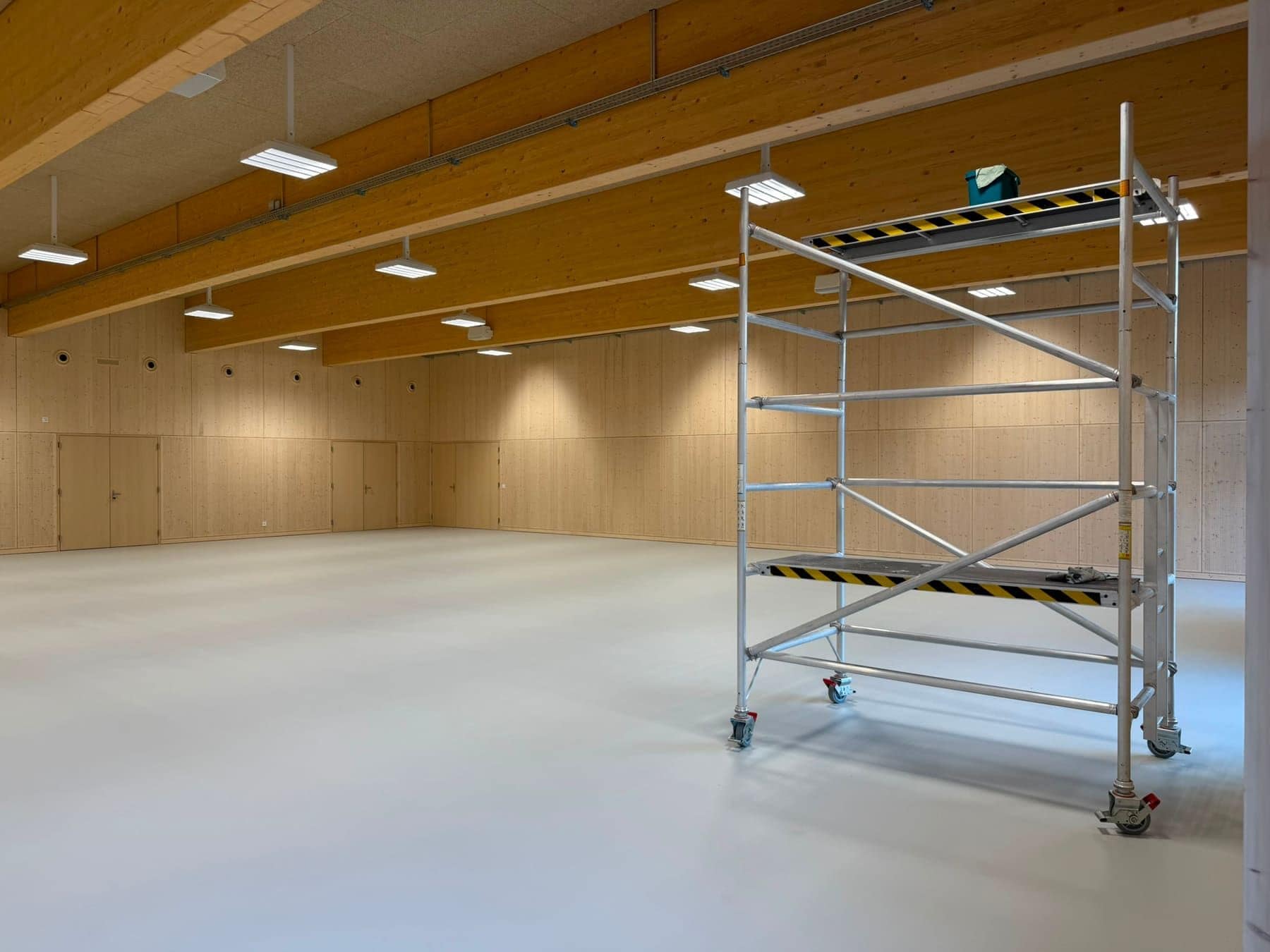 Mehrzwecksaal mit Holzdecke während der Bauendreinigung, ein Rollgerüst steht im Raum