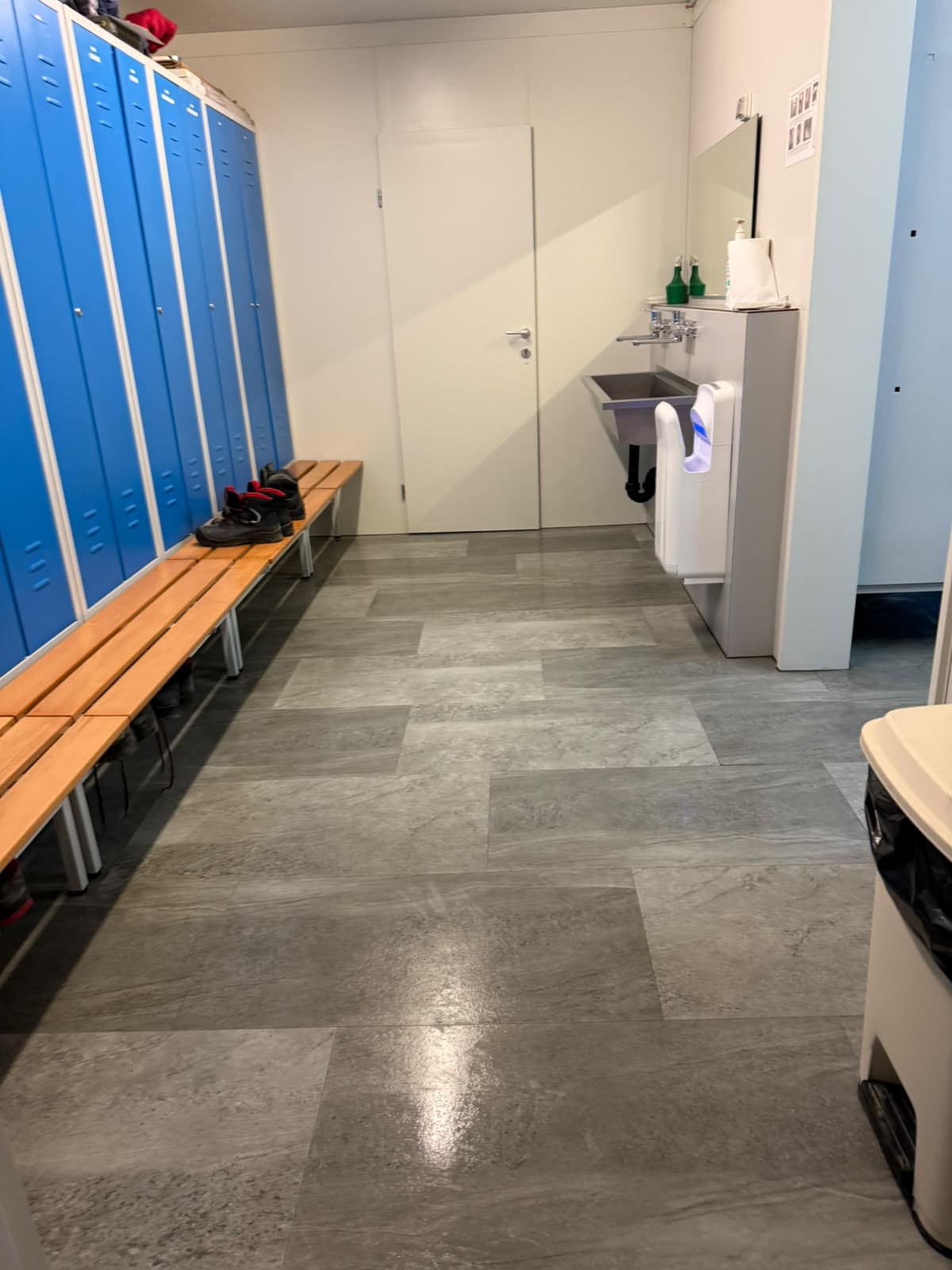 Garderobe mit blauen Spinden, Sitzbank, Lavabo und Plattenboden