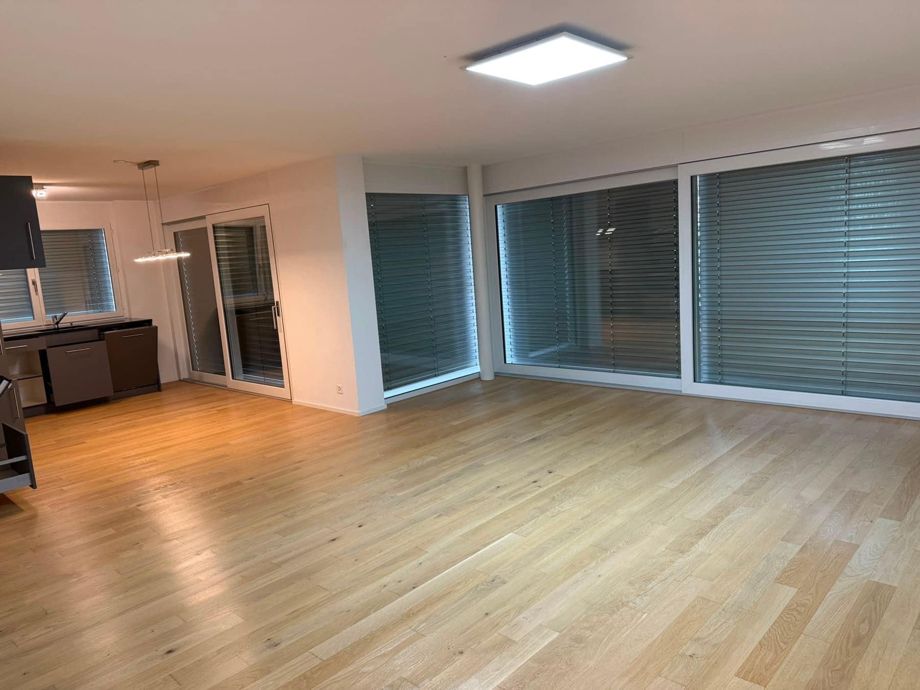 Leeres Wohnzimmer mit grosser Fensterfront und heruntergelassenen Lamellenstoren