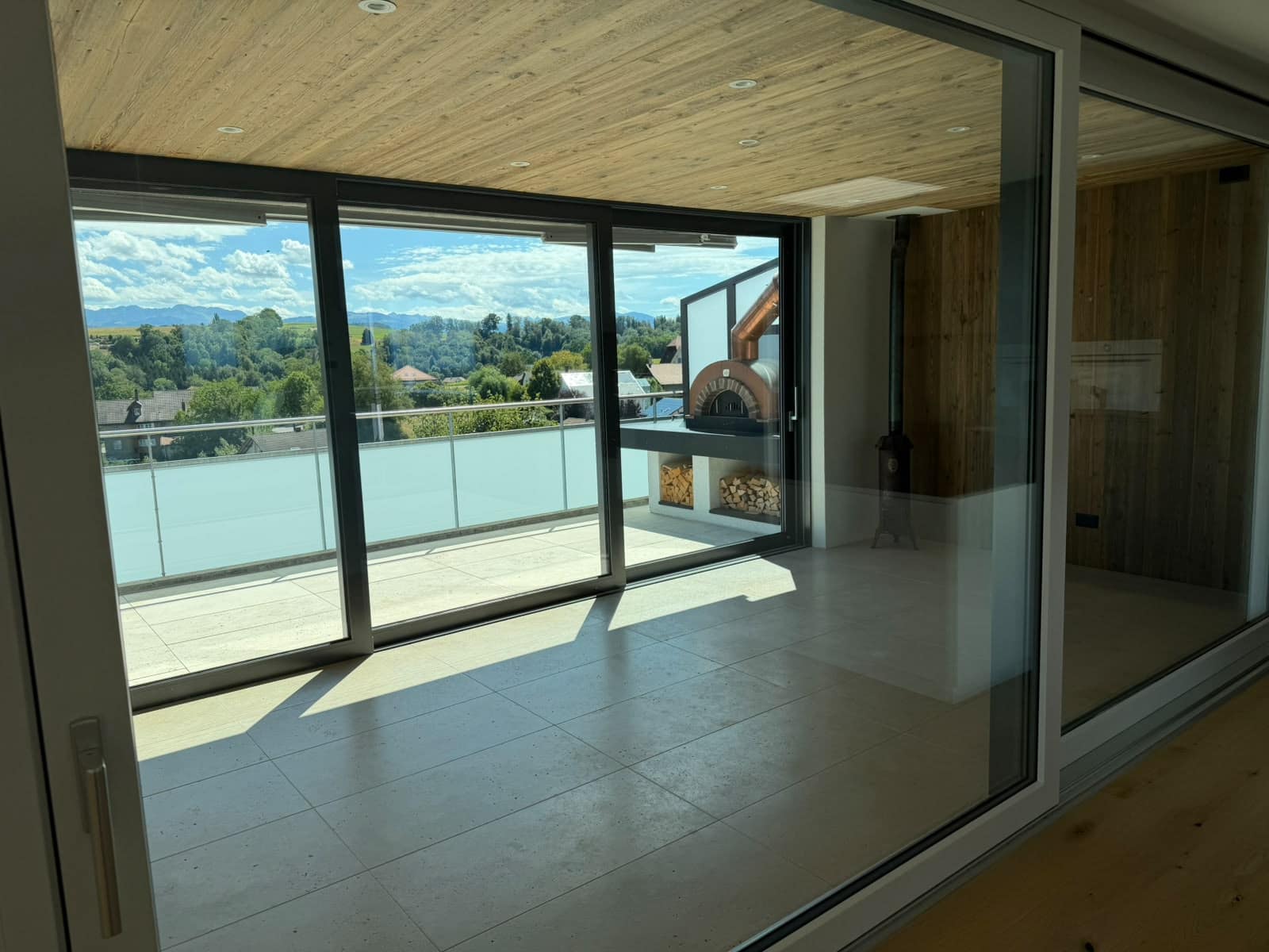 Raumhohe Schiebefenster zu einer überdachten Terrasse mit Glasgeländer