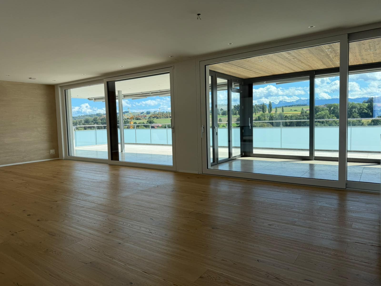 Leerer Wohnraum mit Parkett und zwei Glasfronten zur Terrasse
