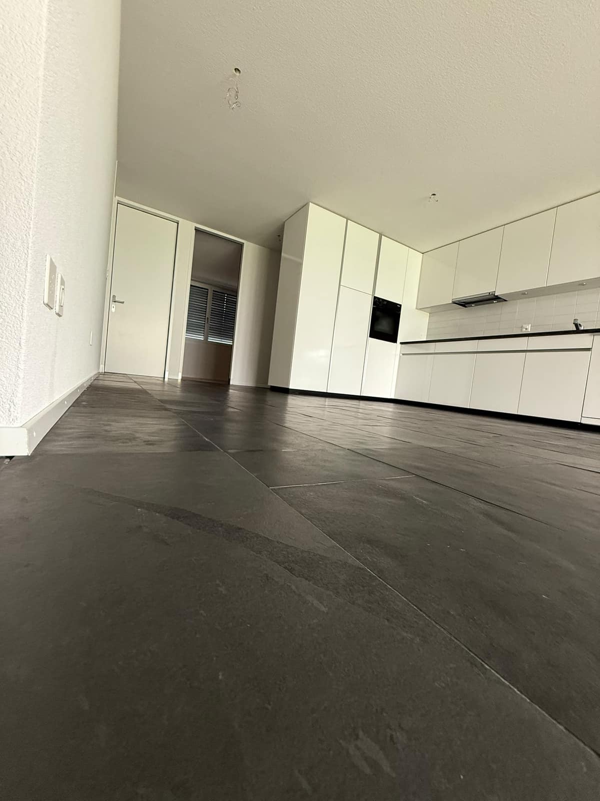 Leere Wohnung mit dunklem Steinboden und weisser Küche